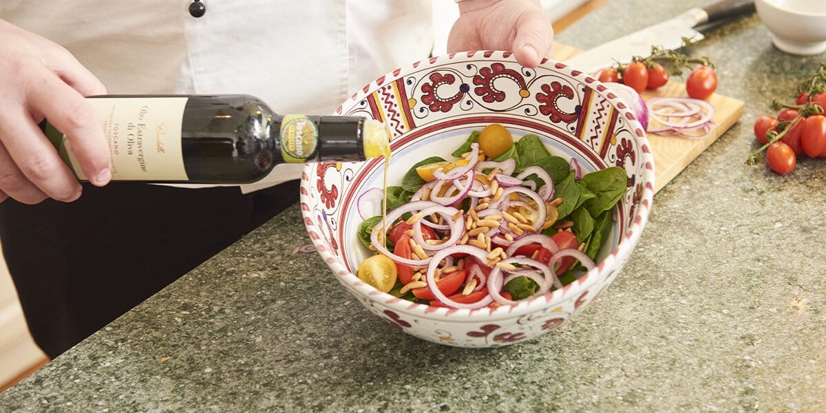 Datteltomaten, Zwiebelringe, Spinat und Pinienkerne in einer Schüssel mit Olivenöl vermischen.